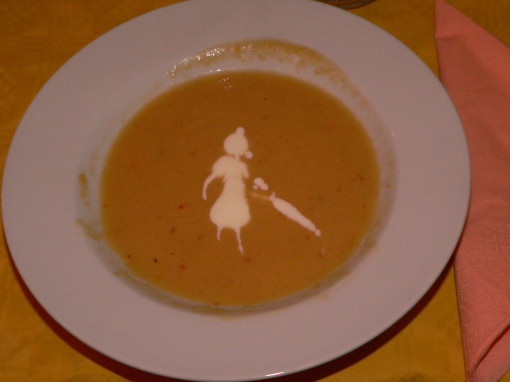 in dem Teller  Kürbissuppe, wurde aus dem Sahnehäubchen das Bild einer Dame mit Regenschirm kreiert  